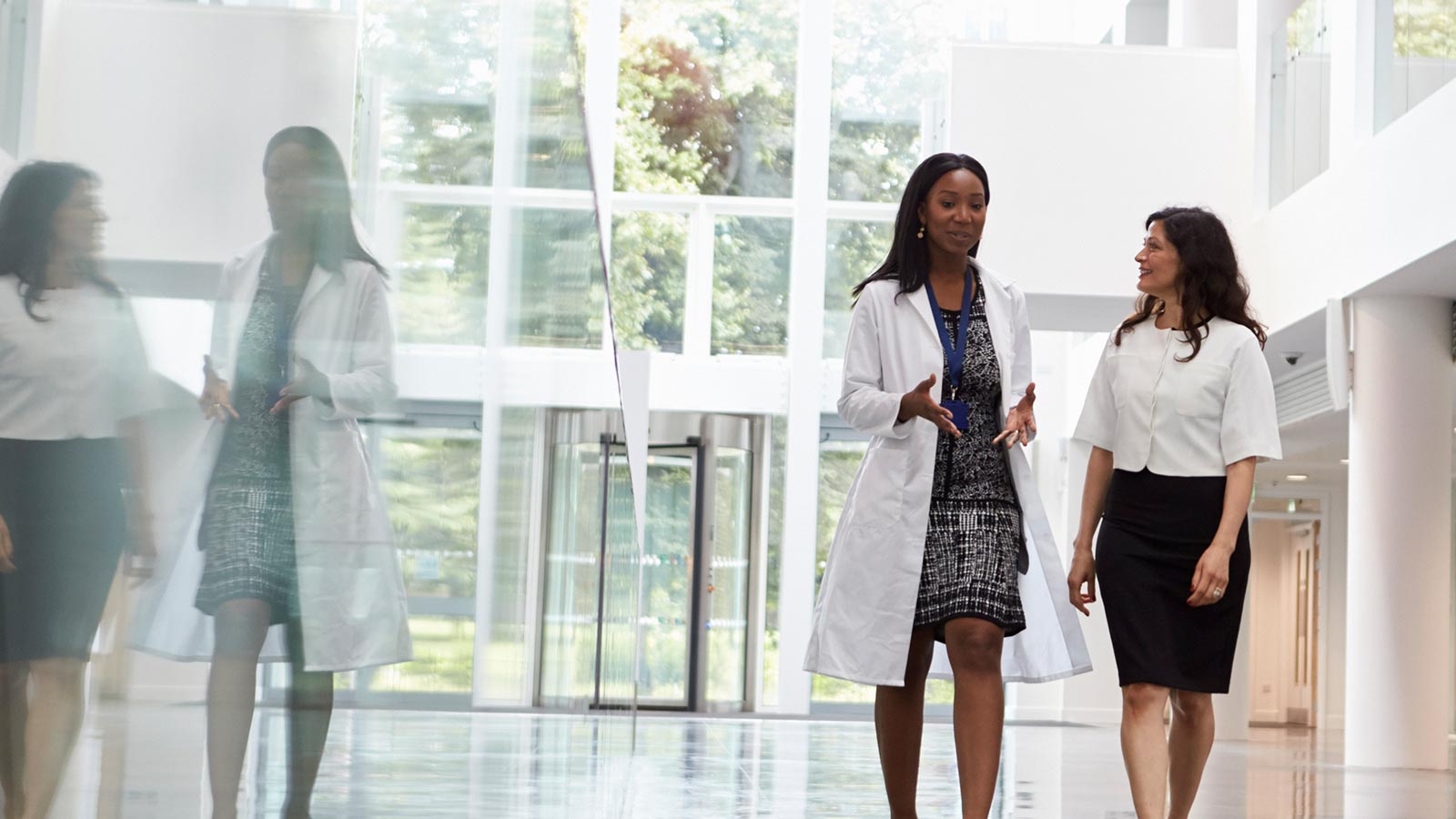 Two doctors walk in an open hallway with bright sunlight
