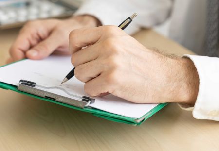 A man holding a pen and writing on a clipboard