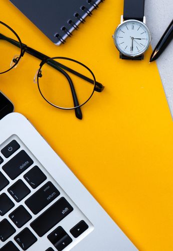 A notebook, glasses, and computer lay on an orange table