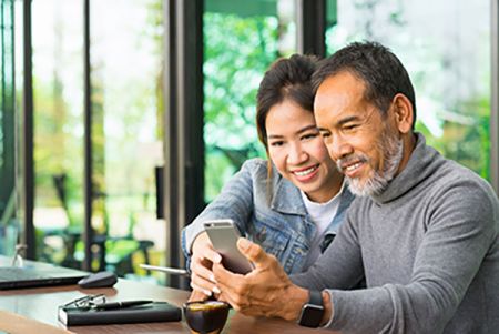 Man smiling at his phone next to his young daughter