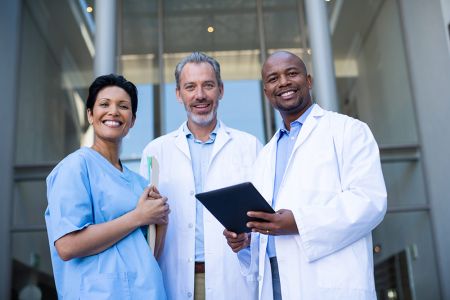 Three professional looking doctors stand and smile at the camera