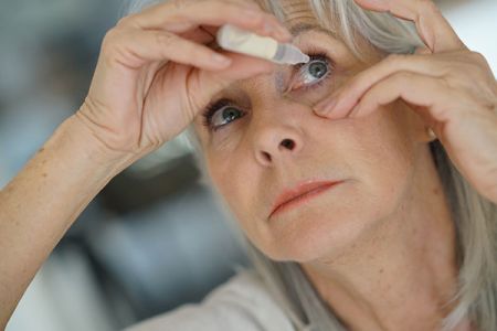 Woman administering eye drops into her own eye